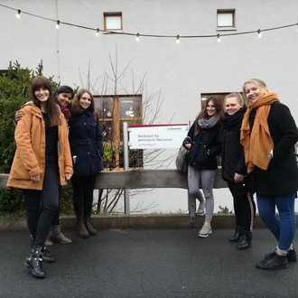 Female students stand in front of the logo of the workshop for people with disabilities in Volmarstein