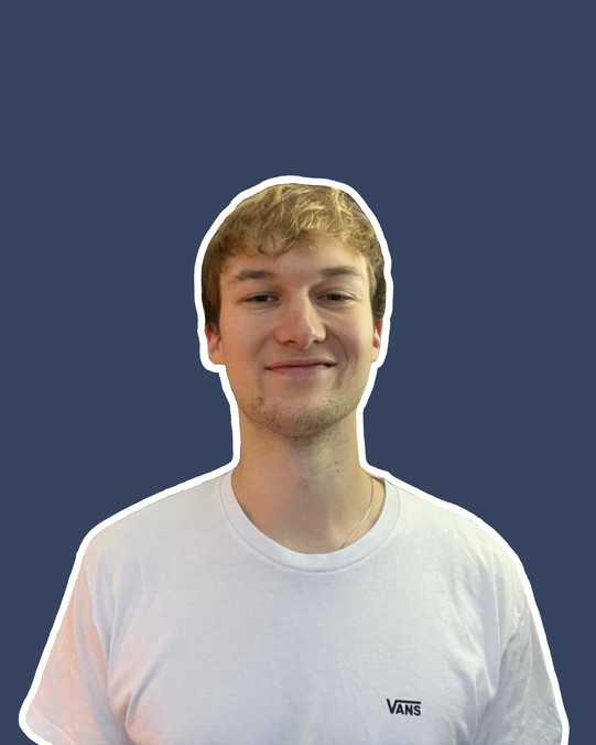 Portraitaufnahme von Tommi Baum, man sieht einen lächelnden Mann mit weißem T-Shirt vor blauem Hintergrund