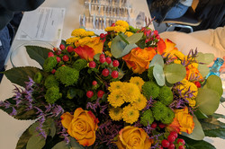 Ein bunter Blumenstrauß liegt auf einem Tisch, geschmückt mit gelben Rosen, grünen Chrysanthemen, roten Beeren und violetten Blüten.