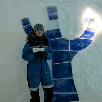 Studentin mit Fakultätslogo vor einer Wand aus Eis in Lappland