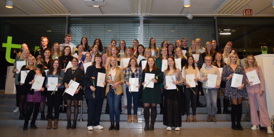 Gruppenfoto der Absolventinnen, Absolventen, Promovendinnen und Promovenden. Alle halten ihre Abschlussurkunden in der Hand.