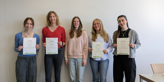 Fünf Frauen stehen nebeneinander von einer weißen Wand. Sie lächeln und halten Urkunden in die Kamera.