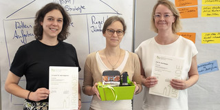 Zu sehen sind 3 Personen Von links nach rechts Jun.-Prof. Dr. Jana Jungjohann, Prorektorin Prof. Dr. Nele McElvany und Prof. Dr. Sarah Weigel, welche Ihre Urkunden und einen Geschenkkorb in den Händen halten. 