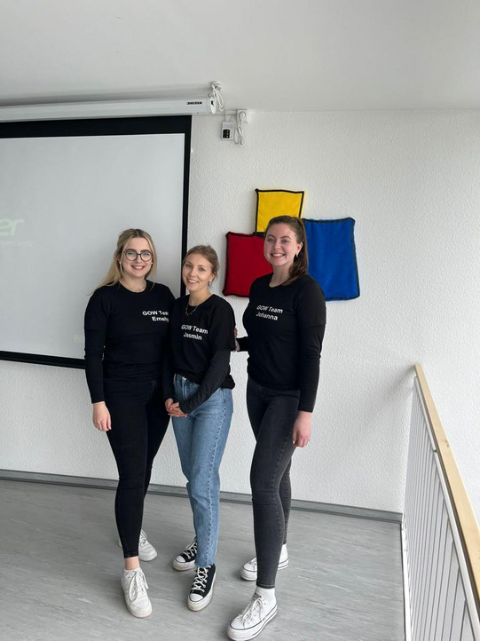 Drei Personen des Bewerbungstrainingsteams stehen in Teamkleidung nebeneinander.