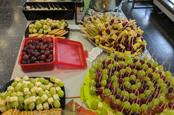 Auf dem Bild ist ein Buffet mit verschiedenen Speisen zu sehen, das auf einem Tisch angerichtet ist. Es gibt eine Vielzahl an Speisen, wie Weintrauben und Käse.