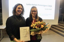 Ein Frau mit Urkunde und eine Frau mit Blumenstrauß schauen feierlich in die Kamera.