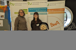 Ein Informationsstand der Technischen Universität Dortmund zeigt das Sprachtherapeutische Ambulatorium und das Bewegungsambulatorium (BwA). Zwei Personen stehen hinter einem Tisch mit Broschüren.