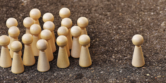 Eine Gruppe von Holzfiguren steht einer einzelnen Holzfigur gegenüber