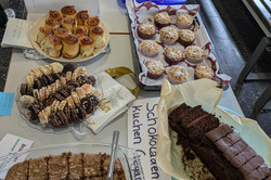 Auf dem Bild ist ein Buffet mit verschiedenen Speisen zu sehen, das auf einem Tisch angerichtet ist. Auf dem Bild ist vor allem Gebäck, wie Schokoladenkuchen zu sehen.