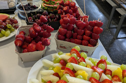 Auf dem Bild ist ein Buffet mit verschiedenen Speisen zu sehen, das auf einem Tisch angerichtet ist. Es gibt eine Vielzahl von Obst wie Erdbeeren und Spießen mit Melone.