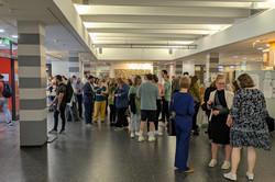 Das Bild zeigt eine Gruppe von Menschen, die sich im Foyer des EF50 versammelt haben. Die Personen stehen in lockeren Gruppen zusammen und unterhalten sich.