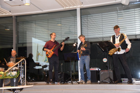 Mitglieder des Jazzquartetts "Jazz Pack" spielen ein Lied. Links sitzt ein Schlagzeuger, zu seiner rechten stehen ein Bassist, ein Gitarrist und ein Saxophonist.