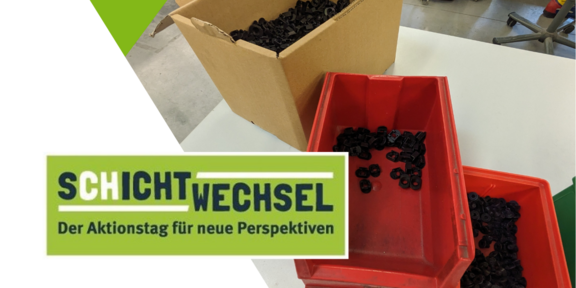 Auf einem Tisch stehen zwei rote Kisten und ein Pappkarton mit schwarzen Muttern. Im Hintergrund sind weitere Kisten und Montagetische zu erkennen. Im Vodergrund der Schriftzug Schichtwechsel.