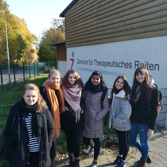 Female students stand in front of the logo of the Center for Therapeutic Riding in Dortmund, Germany