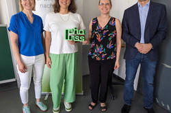 Vier Personen stehen nebeneinander in einem Raum. Im Hintergrund ist ein Roll-Up-Banner mit der Aufschrift „70 Jahre rehawiss – Der Blick zurück nach vorn“ zu sehen. Eine Person hält ein grünes Schild mit dem Schriftzug „rehawiss“ in der Hand. Die Personen sind unterschiedlich gekleidet: eine trägt ein weißes T-Shirt und grüne Hosen, eine andere eine blaue Bluse und weiße Hosen, die dritte Person ein bunt gemustertes Oberteil und schwarze Hosen, und die vierte Person einen dunklen Blazer mit Jeans. 