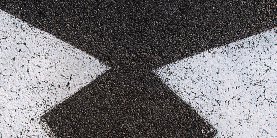 Blick aus der Ego-Perspektive auf eine Straße, auf der zwei weiße Pfeile aufgemalt sind, deren Pfeilspitzen in entgegengesetzte Richtungen zeigen