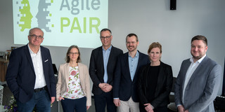 Das Bild zeigt mehrere Personen vor einer Leinwand mit der Aufschrift "Agile PAIR"