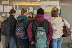 Mehrere Personen stehen vor einem Informationsstand mit dem Banner „Der Paritätische Selbsthilfe-Kontaktstelle Dortmund“. Sie tragen Rucksäcke und unterhalten sich mit den Standbetreuenden.