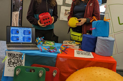 Ein farbenfroher Stand präsentiert Bewegungs- und Therapiehilfsmittel wie große Würfel, Rollenbretter, Bälle sowie Laptop-Präsentationen zum Thema Bewegungstraining.