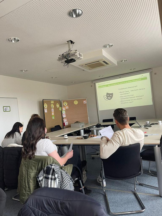 Das Team Datenschutz mit der JVA Iserlohn besprechen sich. Im Hintergrund wird eine Präsentation übertragen.