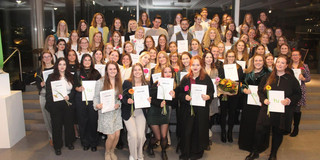 Gruppenfoto von Studierenden auf einer Abschlussfeier. Alle halten Urkunden in den Händen.