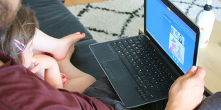 Mann sitzt mit seinem Kind vor einem Laptop und nimmt an der Studie teil