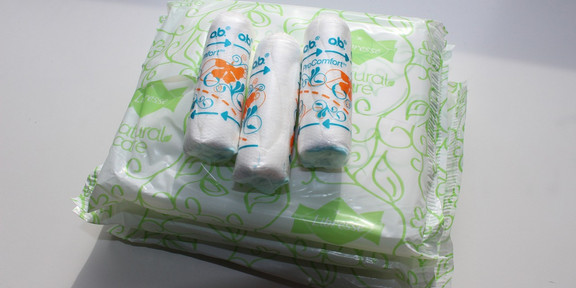 Drei Tampons liegen auf einem Stapel verpackter Binden
