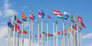 Flag poles with various european flags in front of a blue sky, arranged in a circular pattern