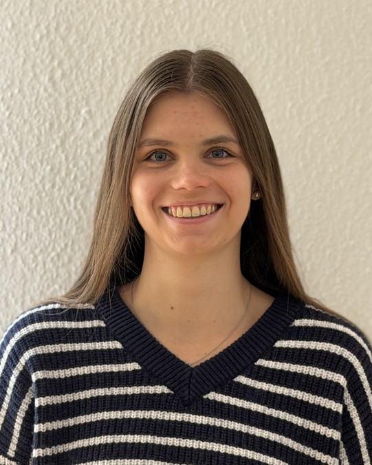 Portraitaufnahme von Sara Tiggelbeck, man sieht eine lachende Frau mit gestreiftem Pullover vor einem neutralen Hintergrund
