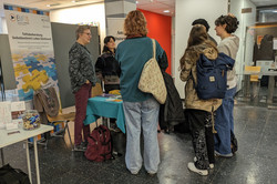 Ein Messestand mit dem Banner „Teilhabeberatung Selbstbestimmt Leben Dortmund“. Mehrere Besucher*innen sprechen mit einer Person am Tisch, auf dem Infomaterialien ausliegen.