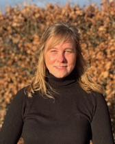 Portraitaufnahme von Julia Hülsken, man sieht eine lachende Frau mit schwarzem Pullover in der Natur