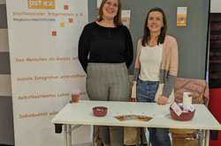 Zwei Personen stehen hinter einem Tisch des psychosozialen Trägervereins e.V. (pst e.V.). Auf dem Tisch liegen Flyer und kleine Schalen mit Werbematerialien, daneben steht ein Roll-Up mit Informationen zur sozialen Integration und Selbstbestimmung.