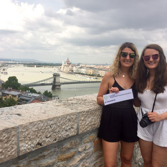 Zwe Studentinnen mit Fakultätslogo auf einer Brücke in Budapest