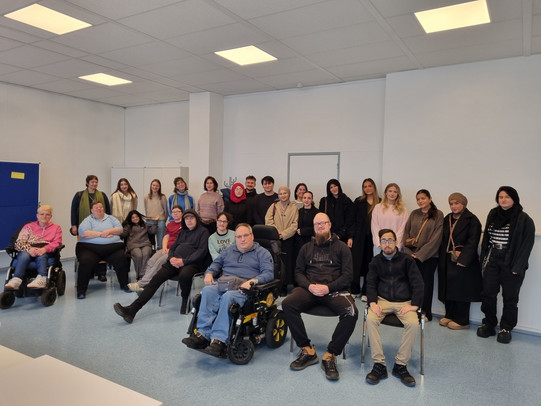 Gruppenfoto mit mehreren Personen, die entweder in der hinteren Reihe stehen oder vorne auf Stühlen sitzen.