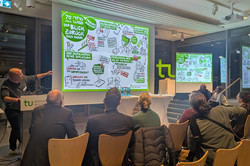 Ein Vortrag findet in einem hell beleuchteten Raum statt. Eine Person steht am Rednerpult der Technischen Universität Dortmund und zeigt auf eine große Leinwand mit einer grafisch gestalteten Präsentation zum Thema Digitalisierung und Inklusion.