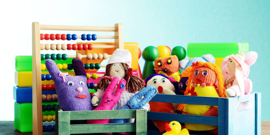 Bunte Handpuppen und Quietscheentchen vor einem Rechenschieber und Bauklötzen.