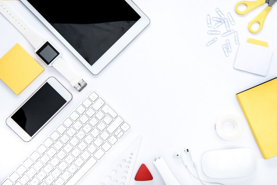 In weiß und gelb gehaltene Gegenstände für die Organisation: Tablet. Büroklammern, Schere, Smartphone, Notizblock, Uhr, Tastatur, Post-It, Thesafilm, Lineal. 