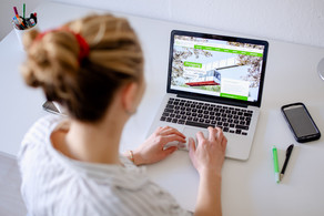 Am Schreibtisch sitzende Studentin tippt auf dem Laptop, daneben liegen Bücher und Stifte.