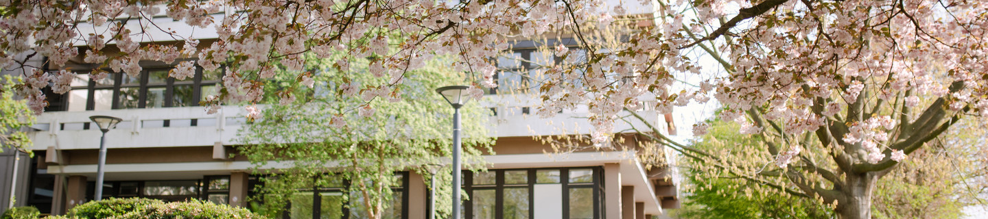 TU Dortmund University building surrounded by flowering trees.