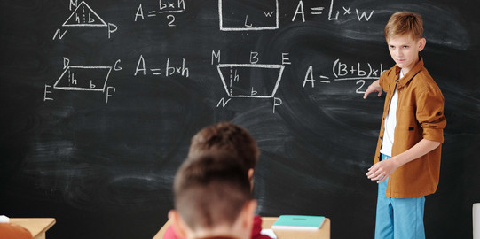 Junge an Tafel Ein Junge steht an der Tafel und erklärt Mathe