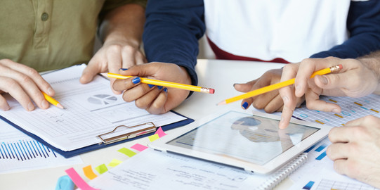 Diagramme_03 Auf einem Tisch liegen Blöcke und Blätter, ein Tablett, welches von einer Hand benutzt wird.